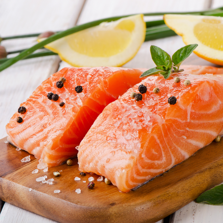 Two cuts of vibrant Ora King Salmon filets seasoned on a wooden board.