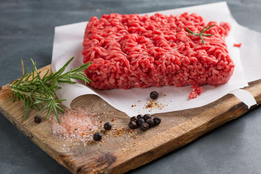 Second City Prime Grass-Fed Angus Ground Beef (1lb) on a wooden board with rosemary and seasonings.