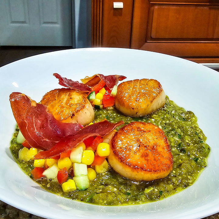 U-10 scallops plated with vibrant vegetables and crispy prosciutto.