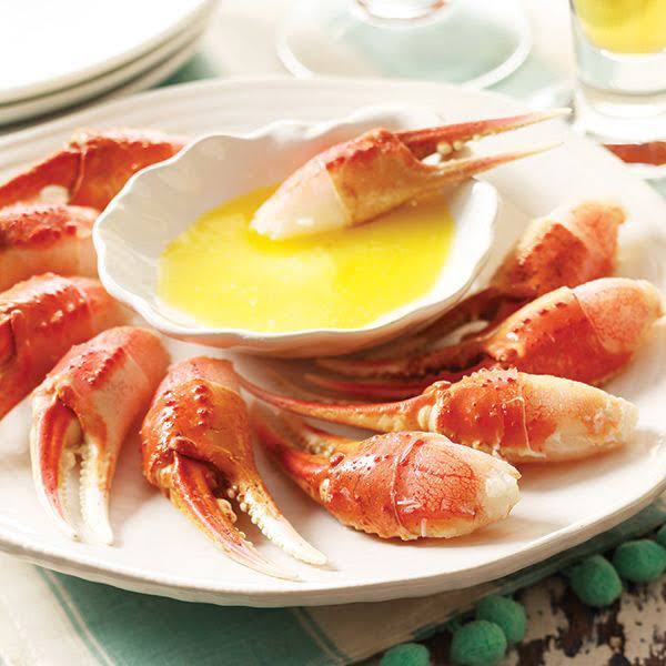 A serving platter with multiple snow crab cocktail claws and a bowl of melted butter.