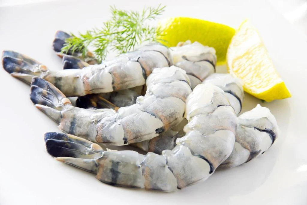 Raw colossal black tiger shrimp (8/12ct) with lemon and dill, ready to cook.