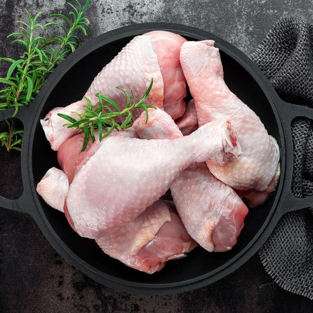 Overhead view of raw Amish chicken drumsticks in a black skillet with fresh rosemary.