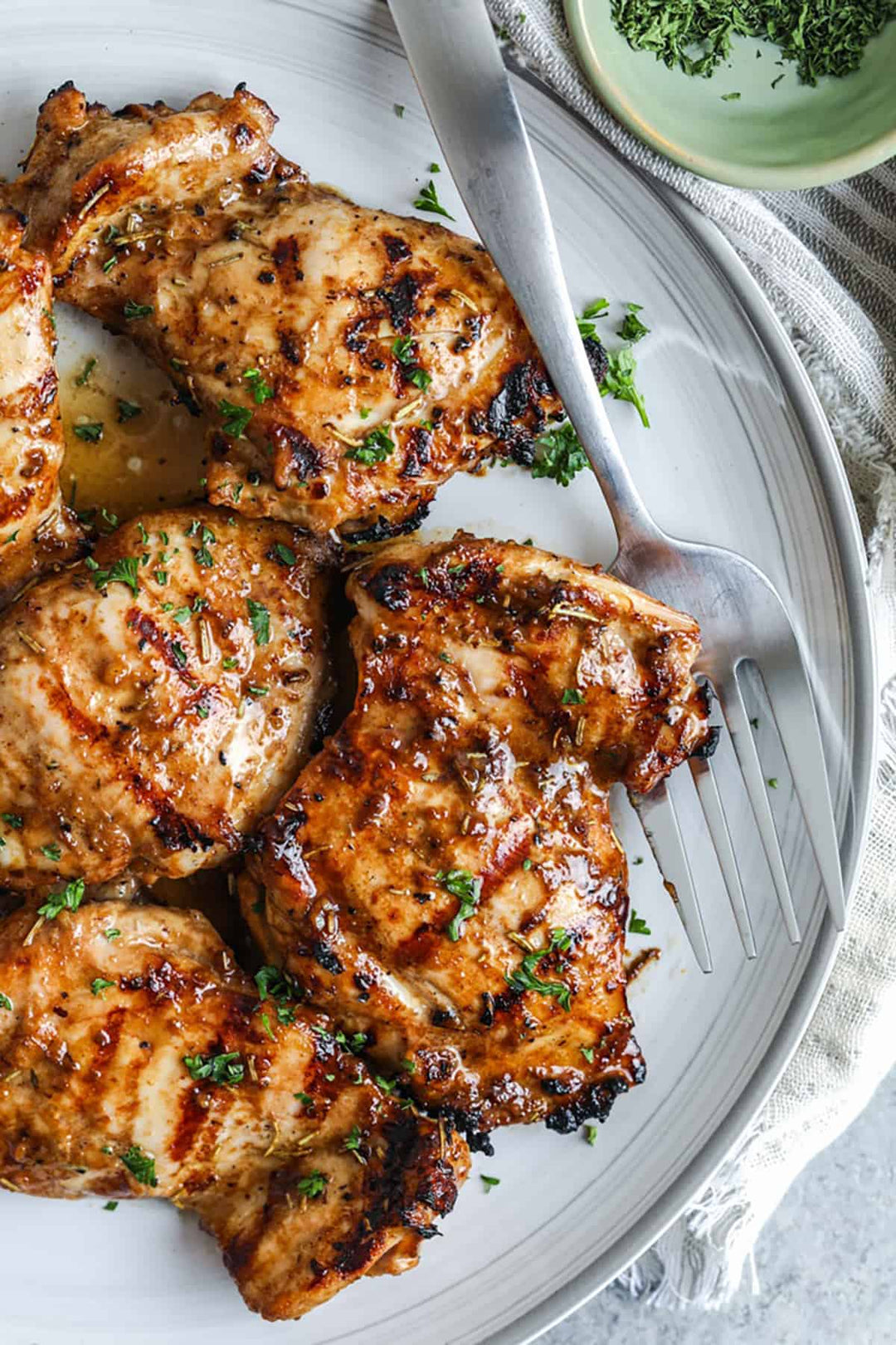Umami Marinated Amish Chicken Thighs, bone-in and skin-on, grilled and garnished with herbs on a white plate.
