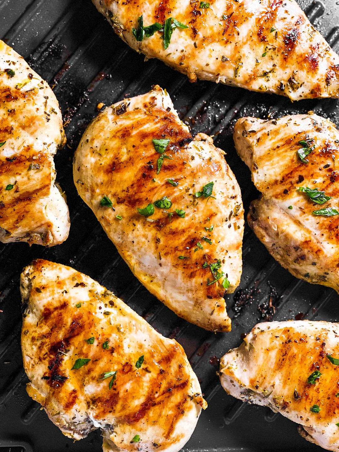 Grilled Green Circle boneless, skinless chicken breasts with herb seasoning on a black grill pan.