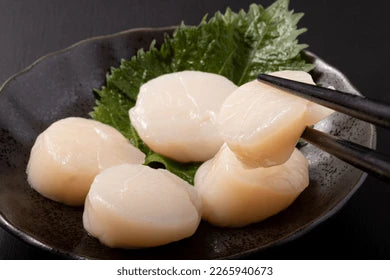 Fresh Japanese Hokkaido Scallops on a plate being picked up with chopsticks.