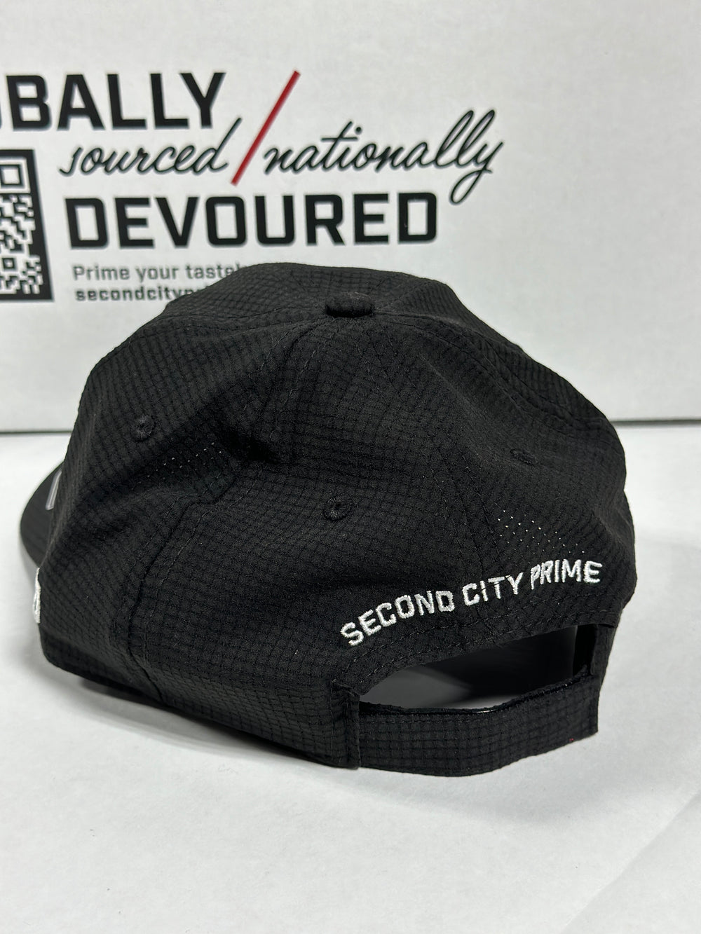 Back of black mesh SCP golf hat with 'Second City Prime' embroidery and adjustable strap.