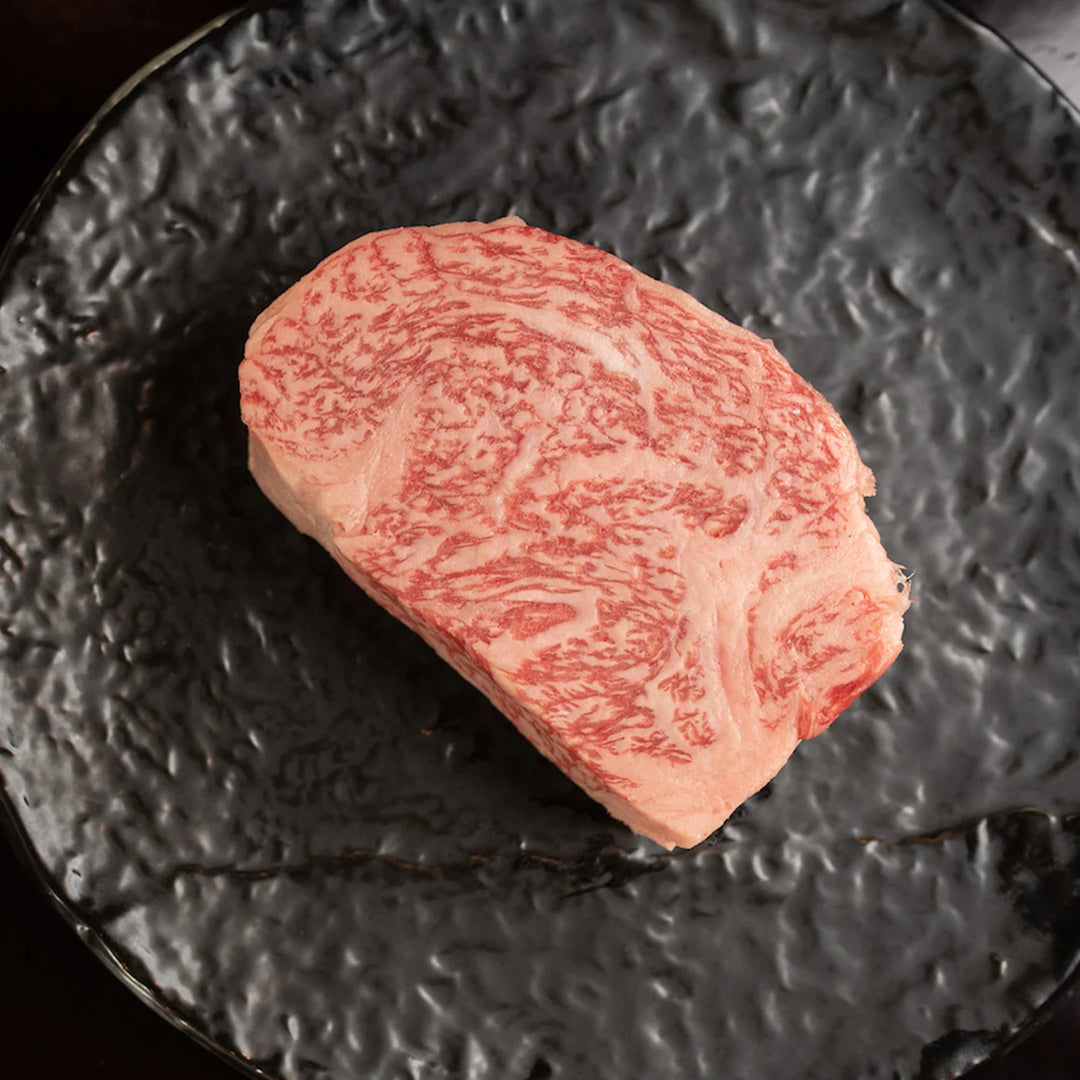 Raw Japanese A5 Wagyu Chuck (Delmonico) Steak showing beautiful marbling on a black plate.