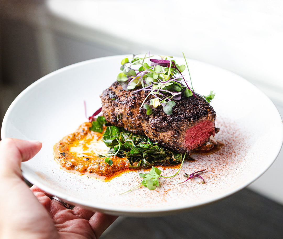 Cooked Bison Filet Mignon plated with greens and garnished with microgreens.