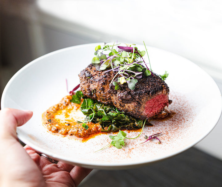 Cooked Bison Filet Mignon plated with greens and garnished with microgreens.