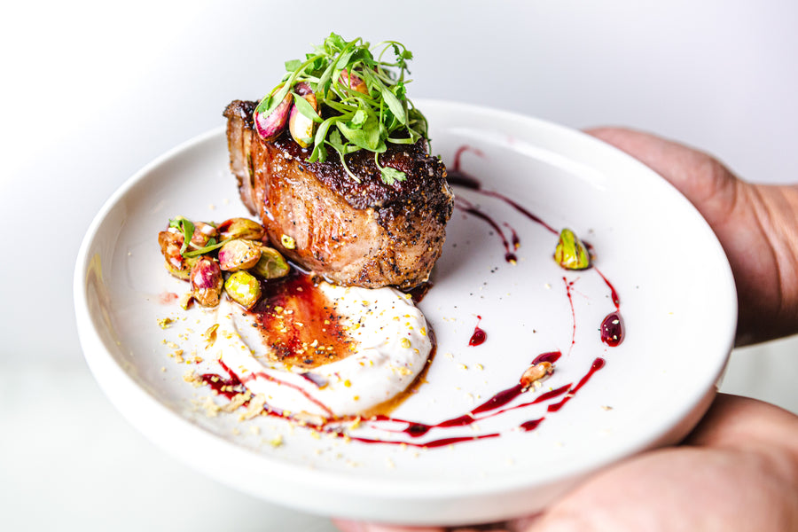 Perfectly seared Domestic Lamb Porterhouse Chop garnished with microgreens and pistachios on a white plate.
