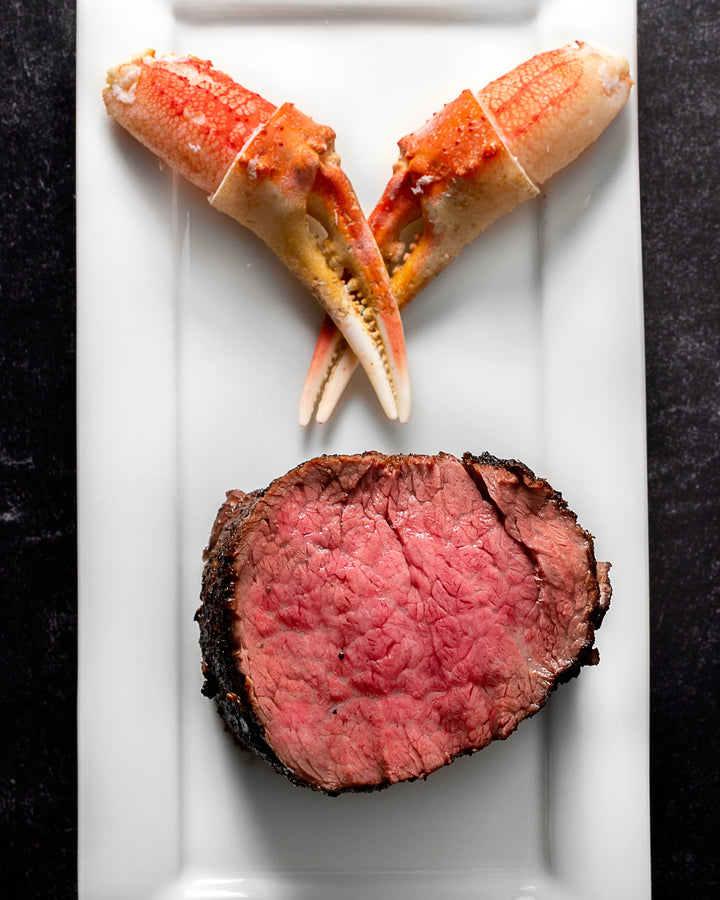 A plate featuring two large snow crab cocktail claws and a slice of pink roasted beef.