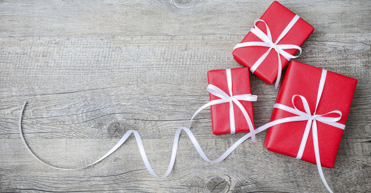 Three beautifully wrapped red gift boxes with white ribbons on a wooden surface.