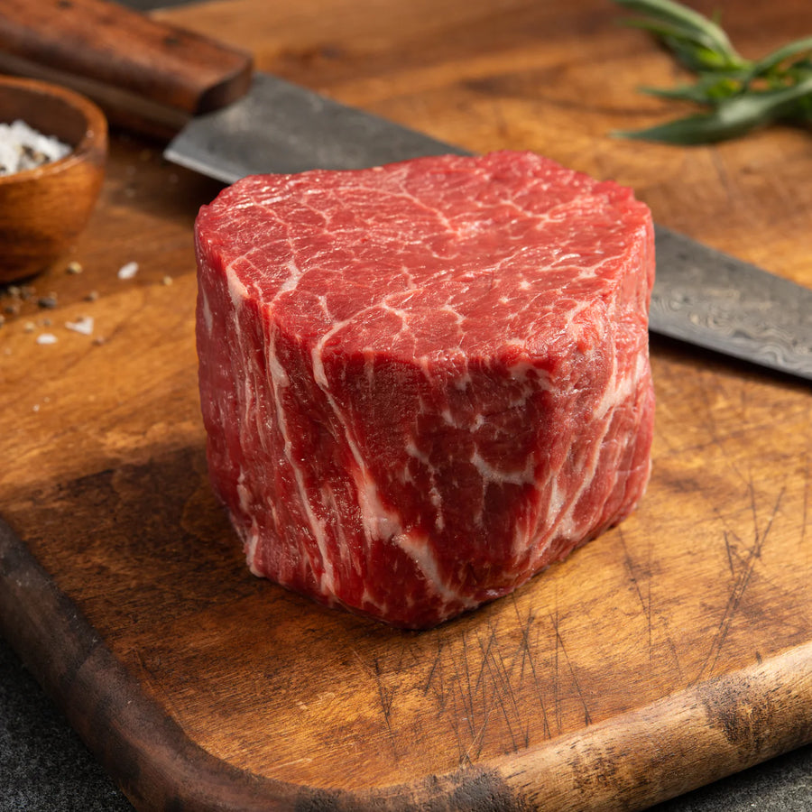 Close-up of a raw, 8oz Grass-Fed Angus PureNZ Boneless Filet steak on a wooden cutting board, showcasing its marbling.