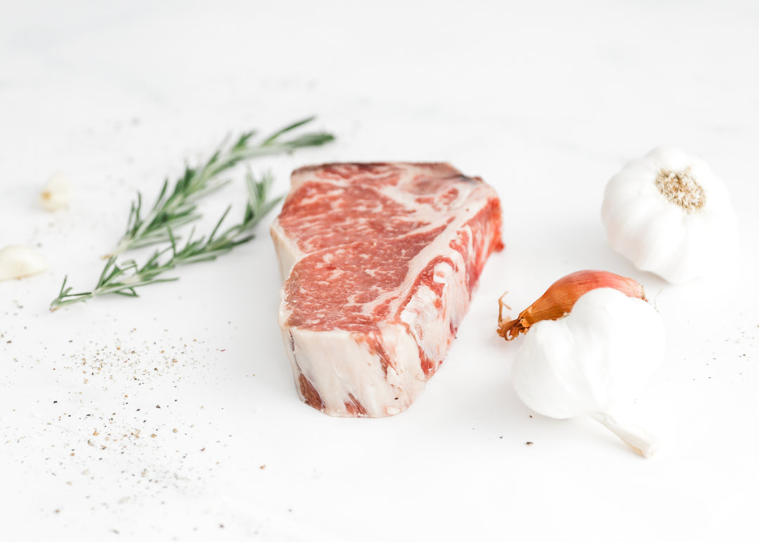 Close-up of a raw, marbled USDA Prime Bone-In New York Strip steak with herbs.