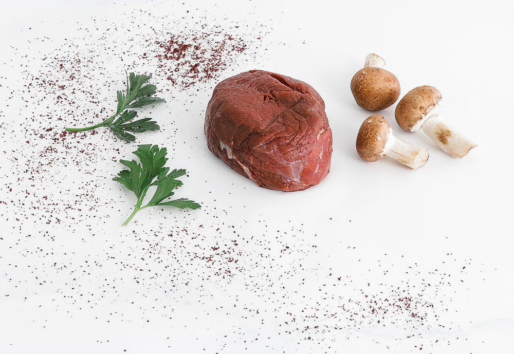 8oz Bison Filet Mignon beside parsley and mushrooms on clean white surface.