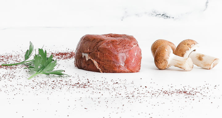 Raw 8oz Bison Filet Mignon with fresh parsley and mushrooms on white background.