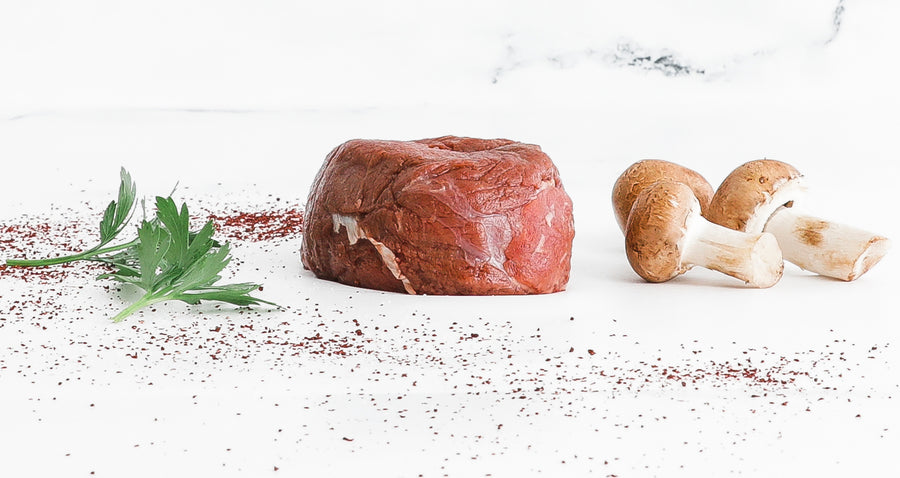 Raw 8oz Bison Filet Mignon with fresh parsley and mushrooms on white background.