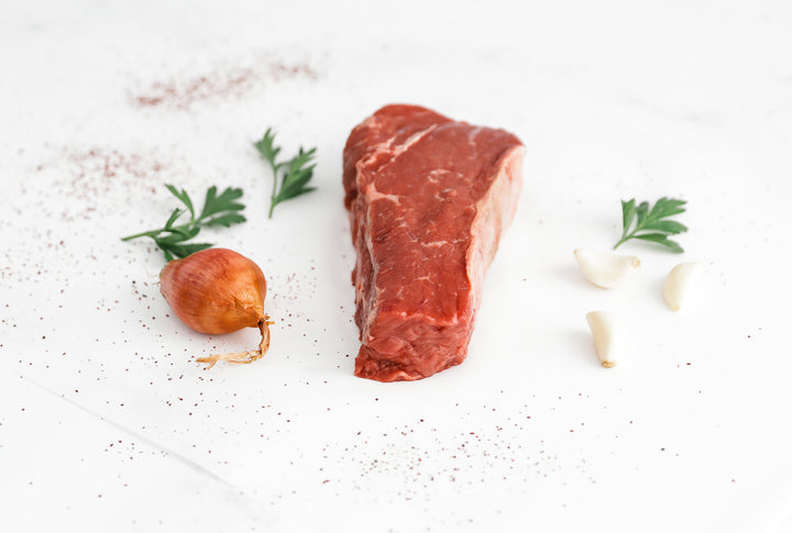 Another angle of a bison NY strip steak with herbs and garlic on a white backdrop.