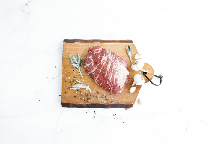 Top view of Iberico Pork Presa on a wooden board with herbs and garlic.
