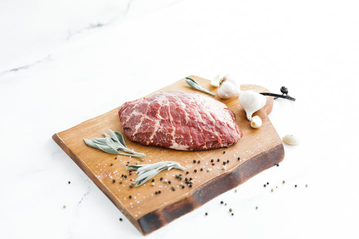 Iberico Pork Presa on a wooden cutting board, garnished with sage and garlic.