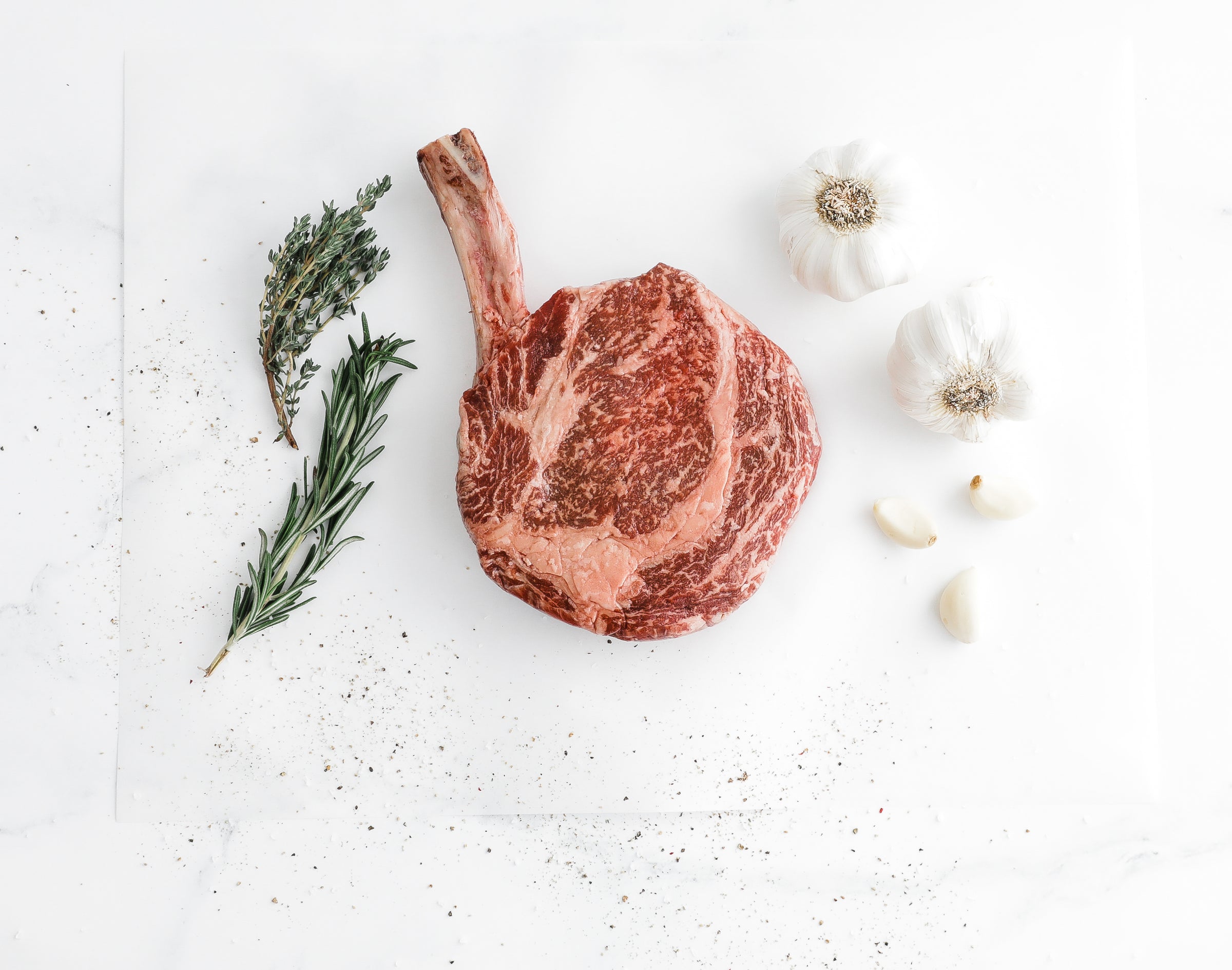 A marbled Australian Wagyu Bone-in Ribeye steak with herbs and garlic on a white background.