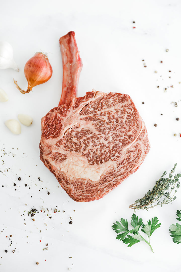 A succulent Australian Wagyu Bone-in Ribeye with intricate marbling, surrounded by garlic and herbs.