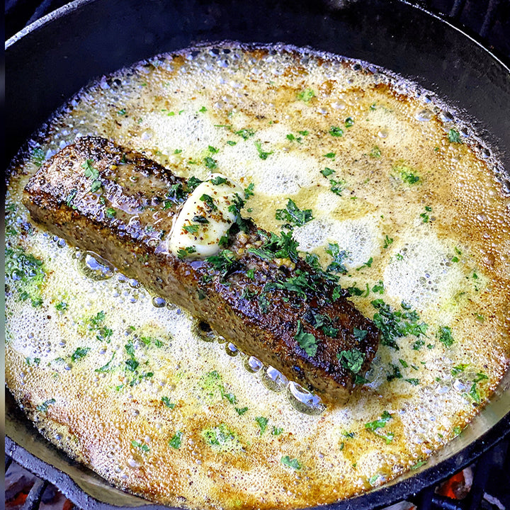 Sizzling Australian Wagyu flank steak in a skillet with butter and herbs.