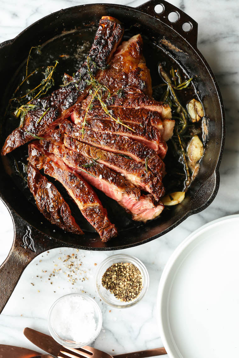 Sliced, juicy grass-fed bone-in ribeye steak in a cast iron skillet with herbs.