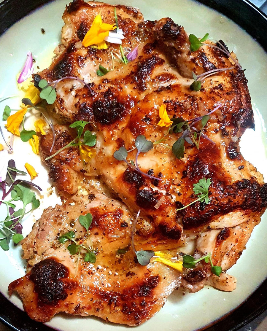 Grilled Amish Brick Chicken garnished with fresh herbs and edible flowers, showcasing a golden brown color.