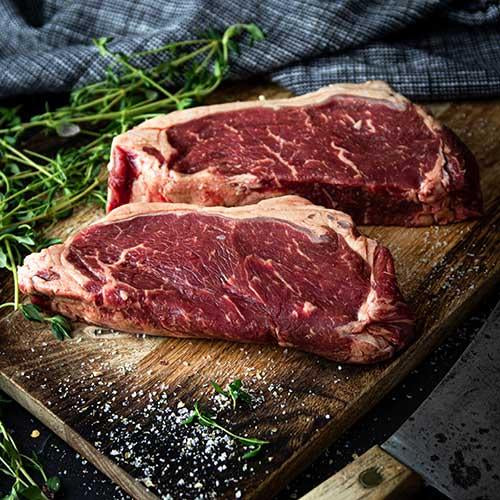 Two Grass-Fed Angus PureNZ NY Strip-loin steaks on a rustic wooden board. High-quality, flavorful, and ready to cook.