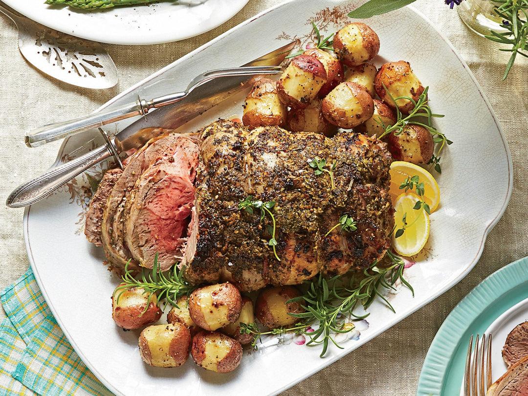 Roasted Colorado boneless leg of lamb with herbs, potatoes, and lemon on a platter.