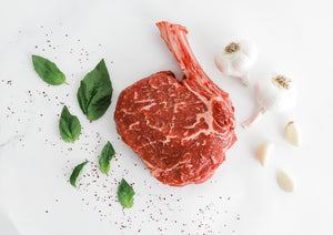 Cut of Prime Bone-in Ribeye from Second City Prime with herbs and garlic.